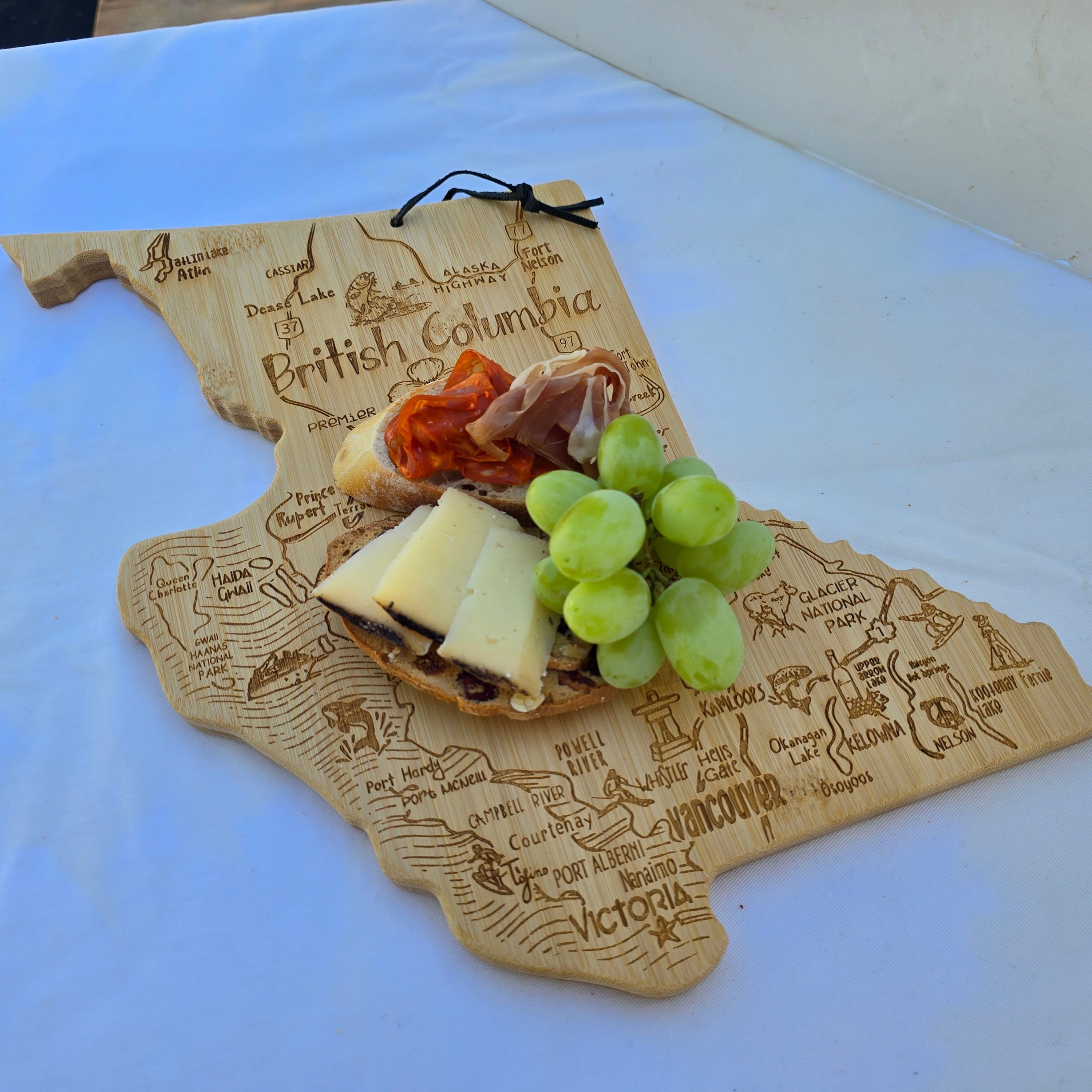 British Columbia Map-shaped cutting board with cheese, grapes, and cured meats on a white surface