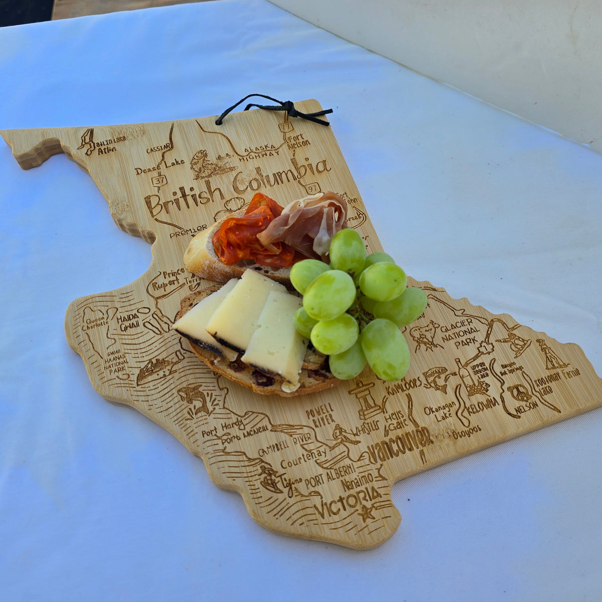 British Columbia Map-shaped cutting board with cheese, grapes, and cured meats on a white surface
