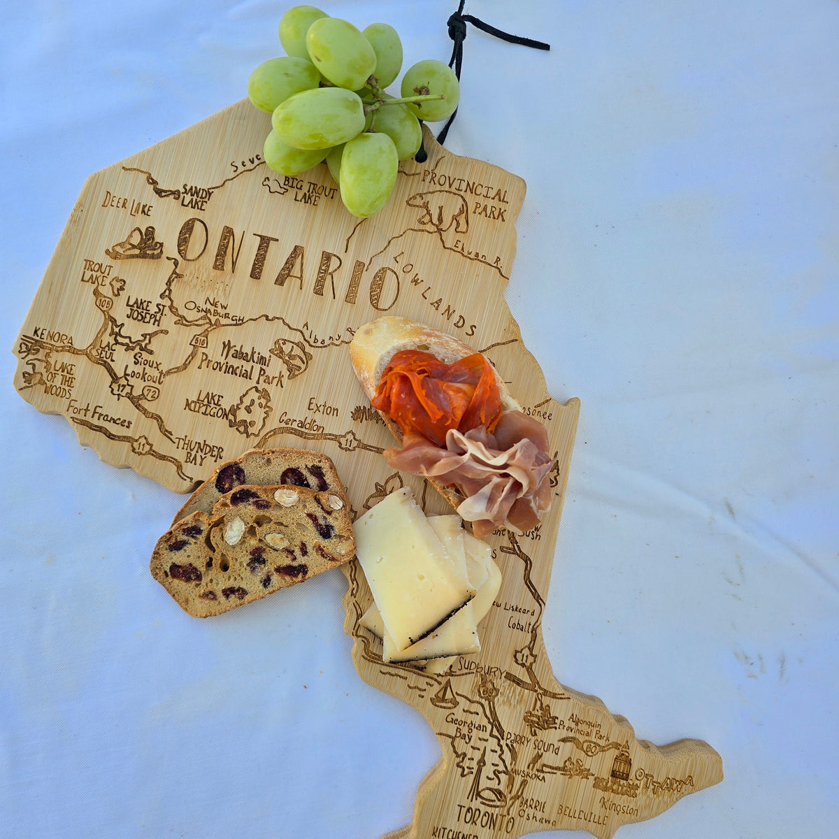 Ontario Map-shaped cutting board with prosciutto, cheese, and grapes on a white plate.